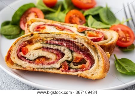 Italian Food Pizza Roll Stromboli With Cheese, Salami, Spinach And Red Pepper A Light Background.