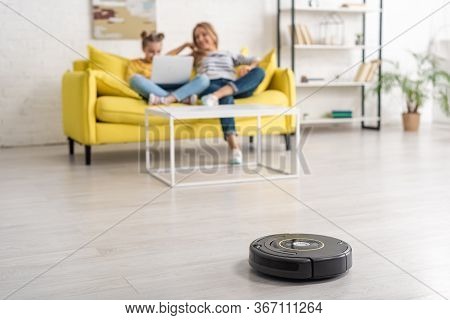 Selective Focus Of Mother And Daughter With Laptop On Sofa Near Coffee Table And Robotic Vacuum Clea