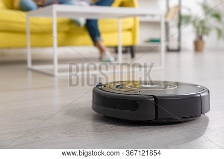 Cropped View Of Mother With Daughter On Sofa And Robotic Vacuum Cleaner On Floor In Living Room