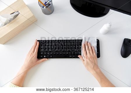 hygiene and disinfection concept - close up of woman hands cleaning computer keyboard with wet wipe