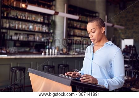 Female Owner Of Restaurant Bar Standing At Counter Using Digital Tablet