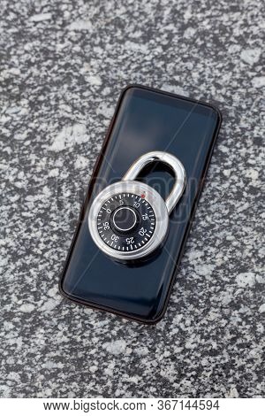 A Modern Black No Name Smartphone And A Shiny Round Simple Combination Padlock Laying On Top Of It, 