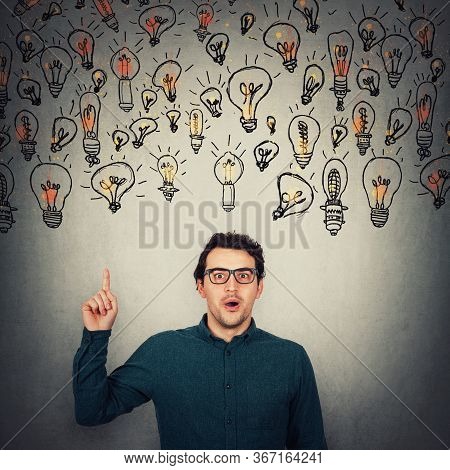 Astonished Businessman, Looking Big Eyes To Camera, Pointing Up Index Finger As Multiple Lightbulbs 