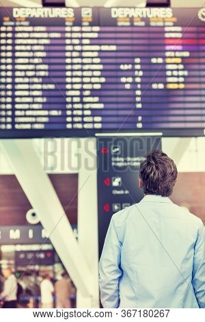 Rear view of mature man looking at his flght on screen in airport
