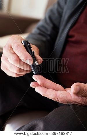closeup of a caucasian senior man about to measure his blood glucose level in a glucose meter by pricking his finger with a fingerstick