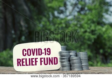 Covid-19 Relief Fund Tag With Stack Of Coins On Wooden Surface