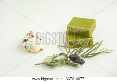 An Olive Branch, A Handmade Olive Soap Bars And Sea Shells On White Background With Copyspace.