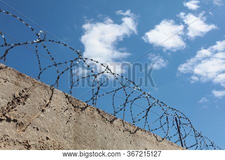 Barbed Wire Over A Concrete Wall. Blue Sky With Clouds. The Concept Of Deprivation Of Liberty Or Res