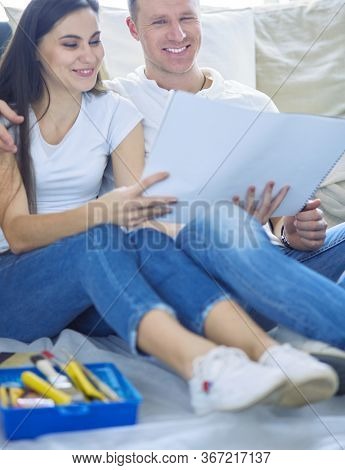 Young couple moving in to new home together, sitting on The floor and diskuss plan of desing.