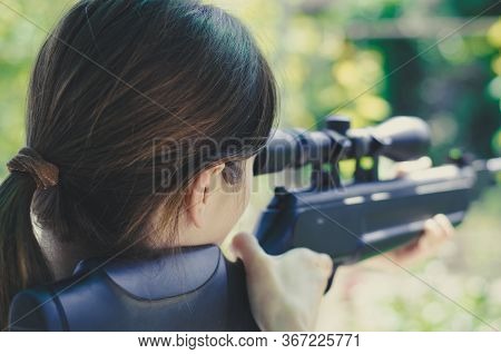 A Girl Looks Into The Scope Of A Sniper Rifle. Back View. Weapons In The Hands Of A Girl. Hunting. W