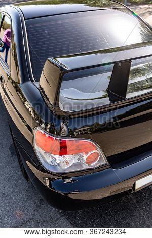Rear Black Shiny Car Spoiler On The Trunk On The Pavement On A Sunny Day. Vertical Orientation.