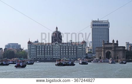 MUMBAI, INDIA - FEBRUARY 15, 2020: Taj Mahal hotel, Gateway of India and tourist boats in water of Arabian Sea on sunset in Mumbai, India