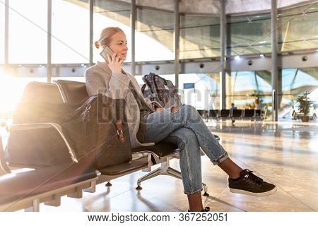Casual Blond Young Woman Using Her Cell Phone While Waiting To Board A Plane At Airport Departure Ga