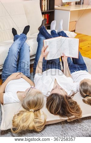 Family Ideas. Portrait Of Caucasian Mother Reading A Book Together With Her Female Twins Laying On F