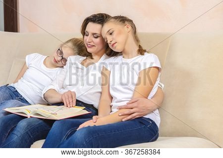 Home Staying Time. Portrait Of Young Caucasian Mother Reading A Book Together With Her Twin Daughter