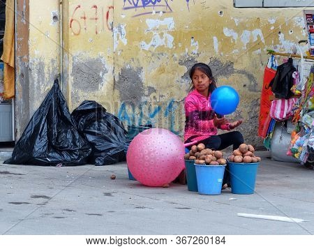 Cuenca, Ecuador - December 23, 2018: Girl From Poor Family Sells Potatoes While Playing With Balloon