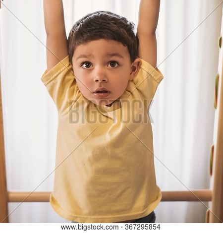 Adorable Child Hanging On Horizontal Bar While Exersicing In Home Gym
