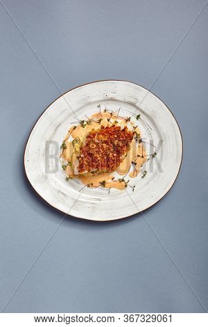 Baked cod fillet with sauce. Restaurant food portion. Fish with batter garnish served on white craft plate. Seafood sprinkled with breadcrumbs meal course. Luxury gourmet dish serving
