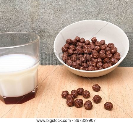 Bowl With Chocolate Balls And A Cup Of Milk On A Wooden Table. Sweet Cocoa, Chocolate, Sugar, Cereal