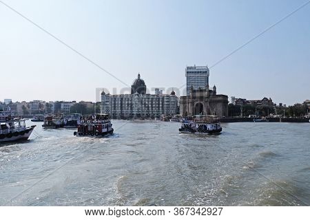 MUMBAI, INDIA - FEBRUARY 15, 2020: Taj Mahal hotel, Gateway of India and tourist boats in water of Arabian Sea on sunset in Mumbai, India
