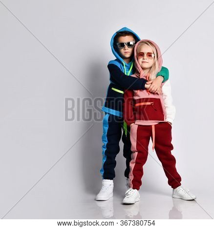 Elder Brother Hugging His Younger Sister. Stylish Sporty Kids In Colourful Tracksuits And Sunglasses