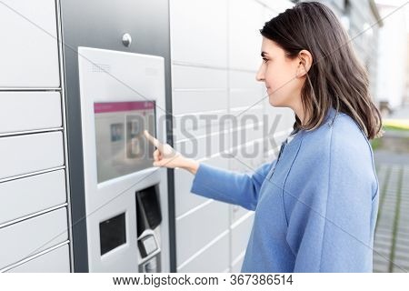 mail delivery and post service concept - woman choosing operation on outdoor automated parcel machine's touch screen