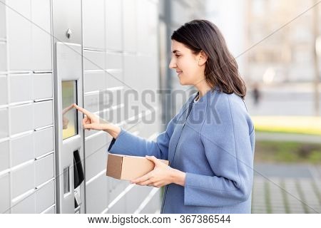mail delivery and post service concept - happy smiling woman with box at outdoor automated parcel machine choosing operation on touch screen