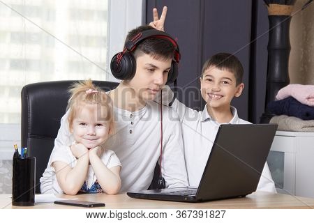 Teenager Looks At A Book And Writes Down A Task And Children Interfere With Learning