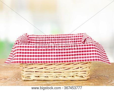 Wicker Basket With A Red Checkered Tablecloth Inside On A Wooden Table