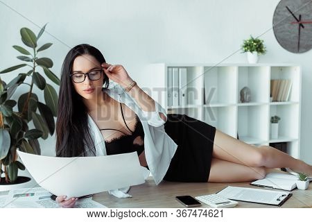 Sexy Secretary In Bra Looking At Document While Lying On Working Table