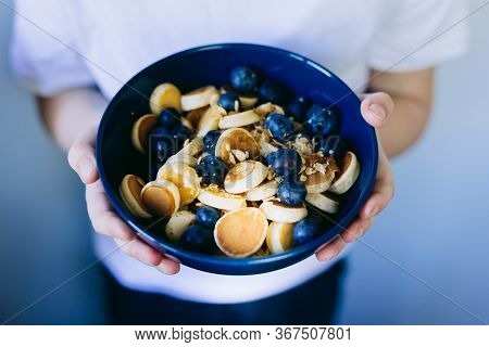 Close- Up Of Mini Pancake Cereal, Mini Pancakes In A Dark Blue Bowl With Maple Sirup Honey With Blue