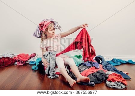 Kid Playing With Clothes On Head. Cute Caucasian Girl Sorting Clothes. Adorable Funny Child Arrangin