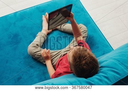 Preschooler Watches Tablet At Home On The Couch. Top View