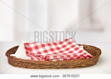 Wicker Oval Basket With A Red Checkered Cotton Napkin Inside And Beige On A White Table