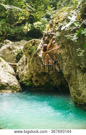 A Woman In A Swimsuit Climbs A Cliff Above The Water, Climbing Over A Mountain River, Bouldering In 