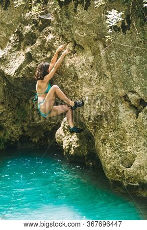 A Woman In A Swimsuit Climbs A Cliff Above The Water, Climbing Over A Mountain River, Bouldering In 