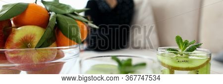 Ecological Natural Fruits On Table And In Drinks. In Background, Girl Is Sitting On Sofa, Waiting At