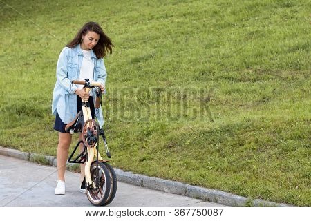 A Beautiful Young Woman Folds Up And Unfolds A Bicycle. Convenient Folding Bike For Travel And Trans