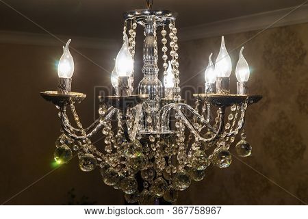 A Crystal Chandelier With Light Bulbs Hangs From The Ceiling.