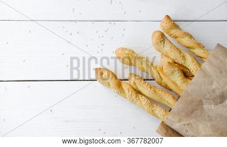 Italian Grissini Or Salted Breadsticks. Sesame Breadsticks In A Craft Paper On White Wooden Table. C