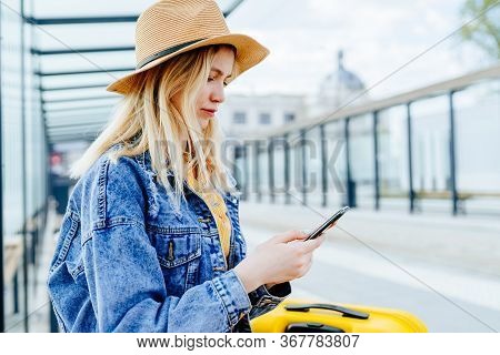 Female Traveler Chatting In Network Via Smart Phone With Her Friends While Sitting On Bus Stop In Su