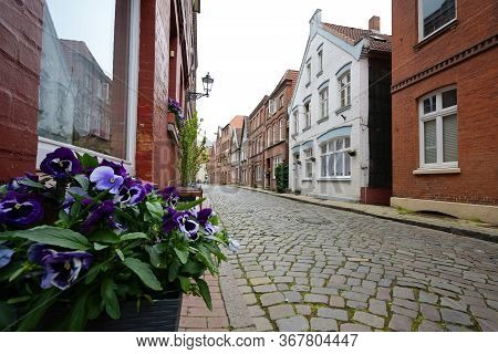 Lauenburg, Germany, May 23, 2020: Old Town Alley With Cobblestones, Historic Houses And A Flowerpot 