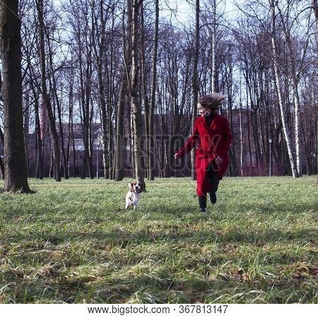 Pretty Young Girl In Redd Coat Playing With Dog Outside In Green Park, Lifestyle People Concept