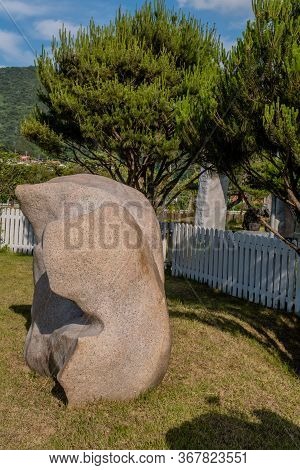 Large Granite Boulder In Front Of White Picket Fence In Public Rock Garden.
