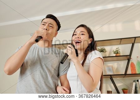 Cheerful Talented Young Couple Singing Songs In Microphones Together At Home