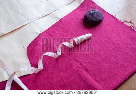 A Paper Pattern Of Trousers, A Needler, And A Centimeter-long Ribbon Lie On A Red Cloth On The Table