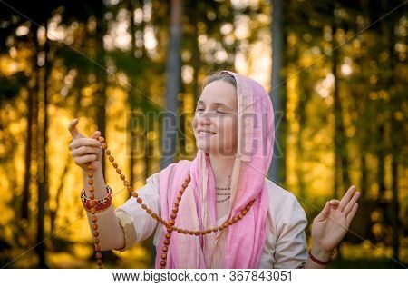 Woman In Indian Clothes In Sunny Forest Meditating And Smiling With Rosary In Hands