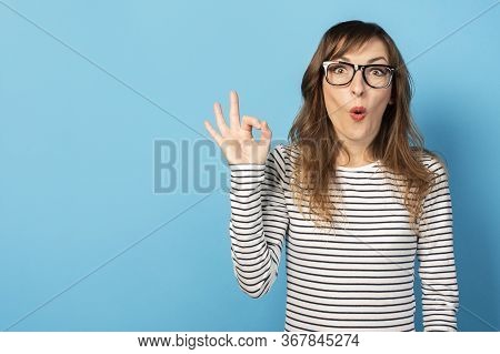 Portrait Of A Young Friendly Woman With A Surprised Face In A Casual T-shirt And Glasses Makes An Ok