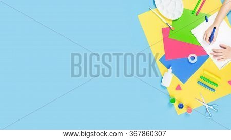 Hands Drawing Over Color Paper, Scissors, Pencils Paint And Various School Stationery On Blue Yellow