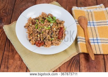 Cooked Paella With Meat And Mushroms On The White Dish And Wooden Spoon On Napkin On The Rustic Tabl
